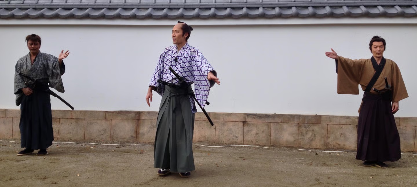 A traditional samurai demonstration in Japan, with three performers in front of a tiled wall